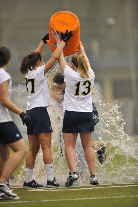 Jane Stoeckert (27) and Julie Foote (13) douse head coach Tracy Coyne with a Gatorade shower following Notre Dame's 16-4 win over Duquesne.  The victory was the 100th in the program's history and Coyne's 100th as head coach of the Irish.