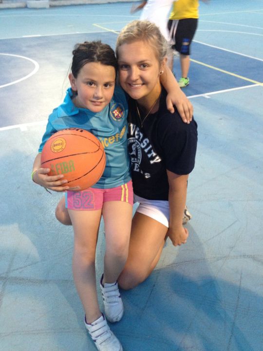 Freshman volleyball student-athlete Rebecca Nunge with a village child on an outdoor basketball court in Ancient Corinth, Greece.