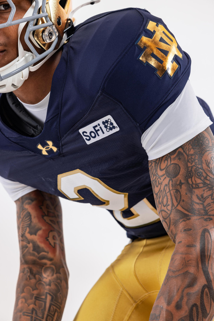 Close-up of a Notre Dame football player wearing the new SoFi jersey patch on the sleeve of the team's navy Under Armour uniform.